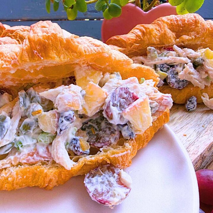 A side view of a croissant sandwich filled with a Waldorf chicken salad. There is another in the background.