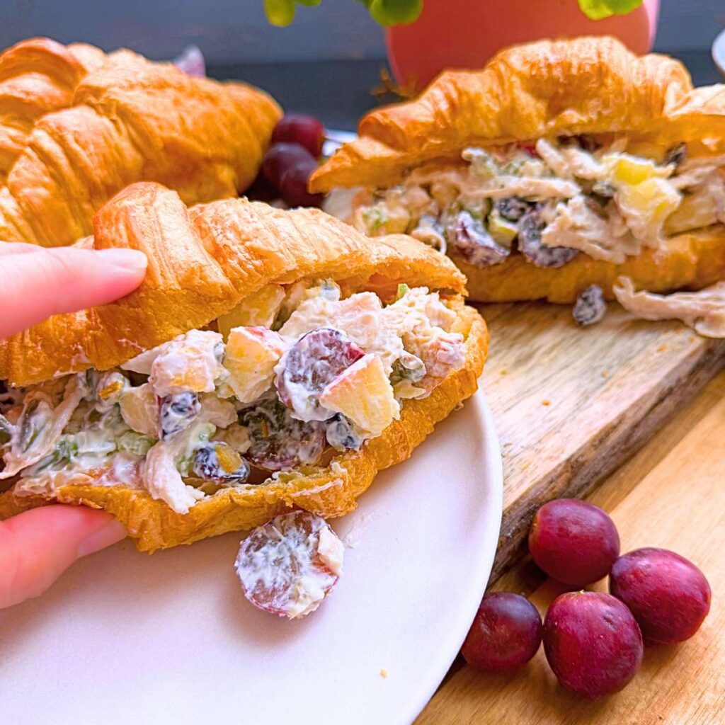 Two croissants filled with Waldorf chicken salad filling. There are purple grapes in front.
