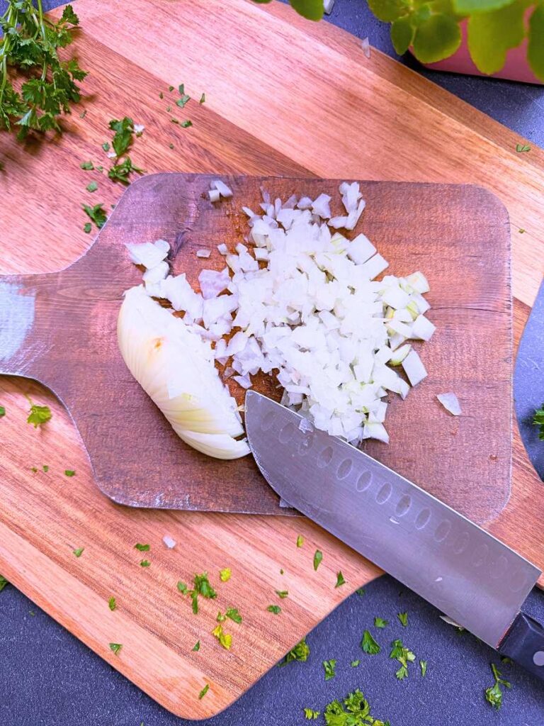 A cutting board with a partially chopped onion and a knife.