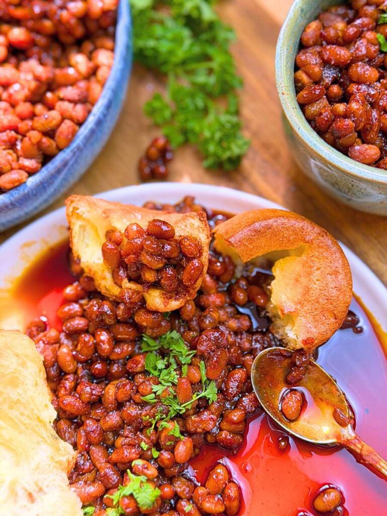 A plate of baked beans with a popover on the plate. There are two more bowls in the background with baked beans inside.