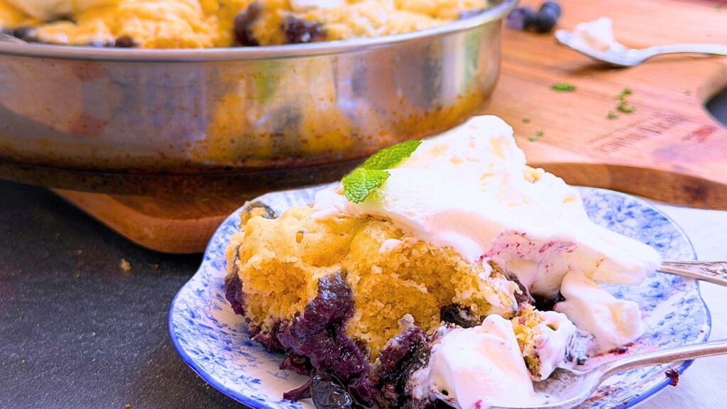 A serving of blueberry grunt with vanilla ice cream on a plate. There is more in the background.