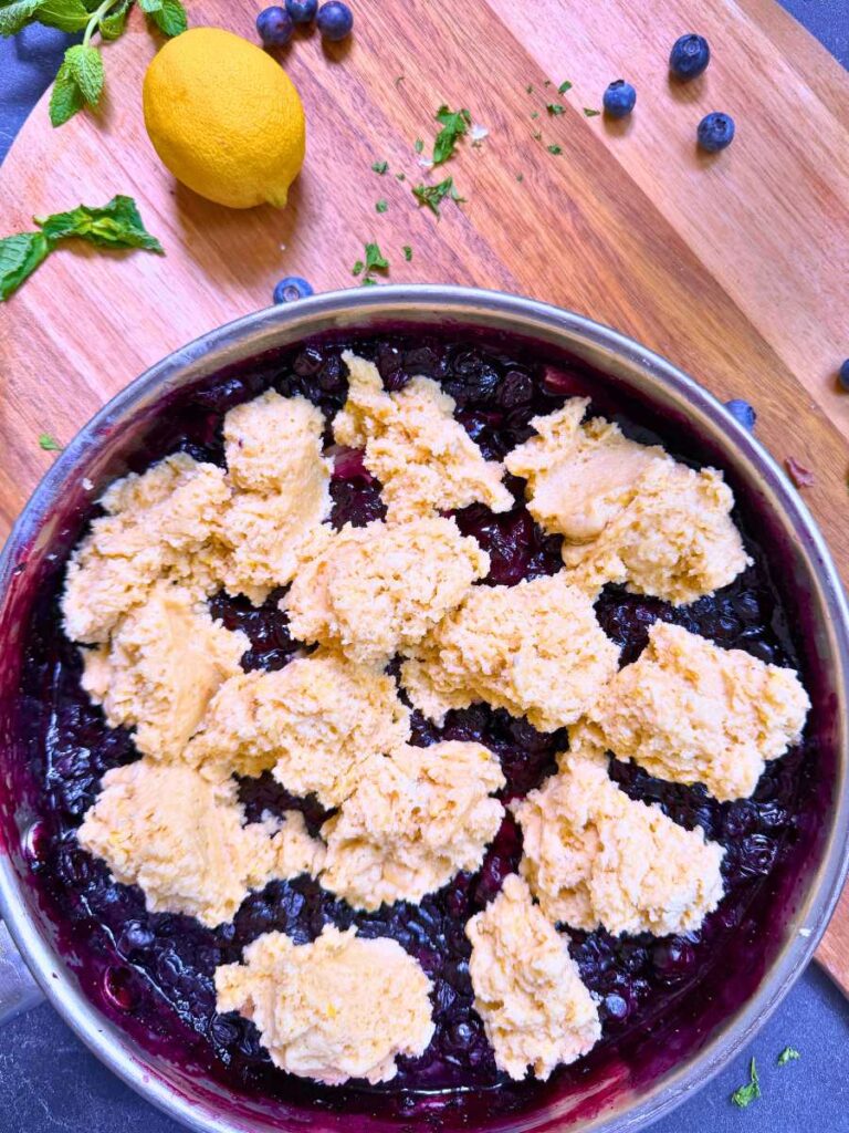 A metal pan with a blueberry sauce and biscuit batter on top.