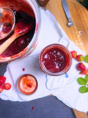 A jar of strawberry jam being filled. 