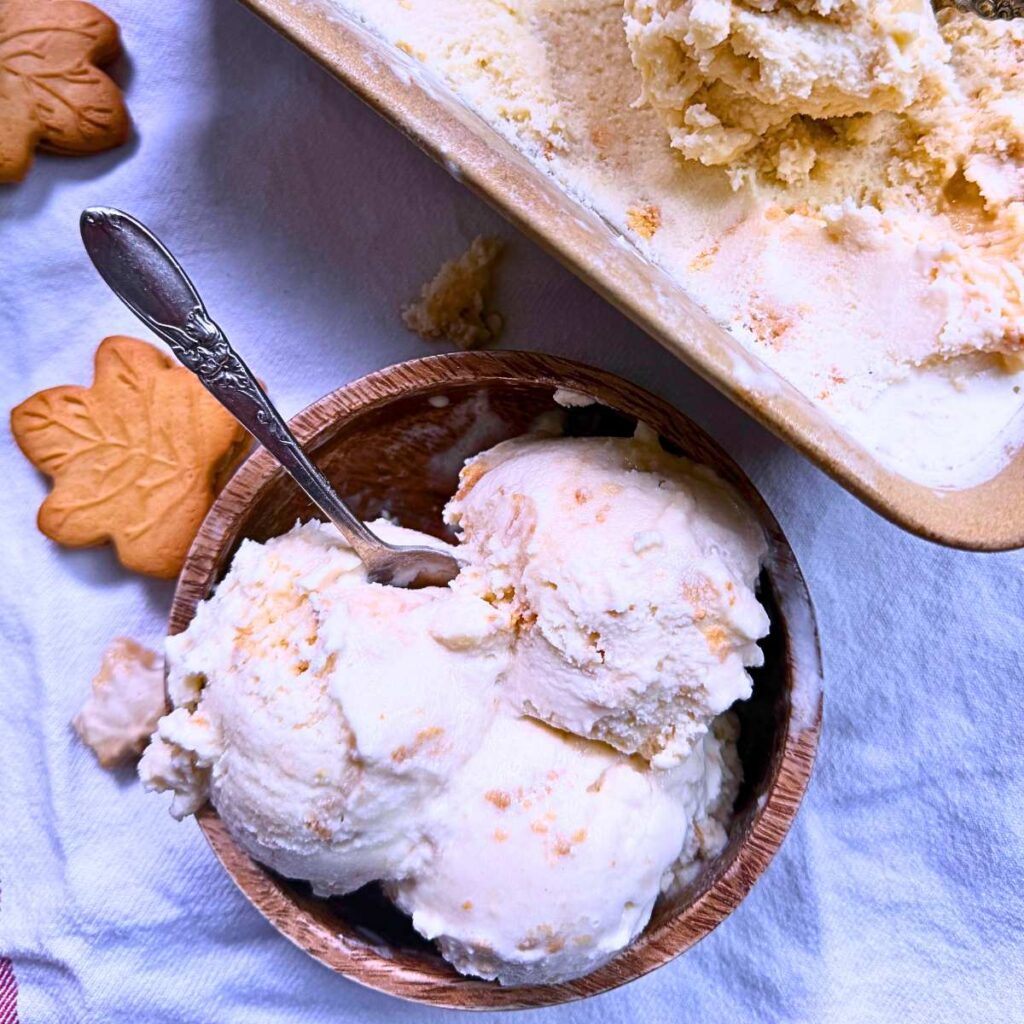 A wooden dish of maple ice cream with a spoon inside. There is more in the background.