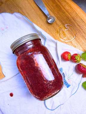 A closed jar of strawberry jam on it's side.