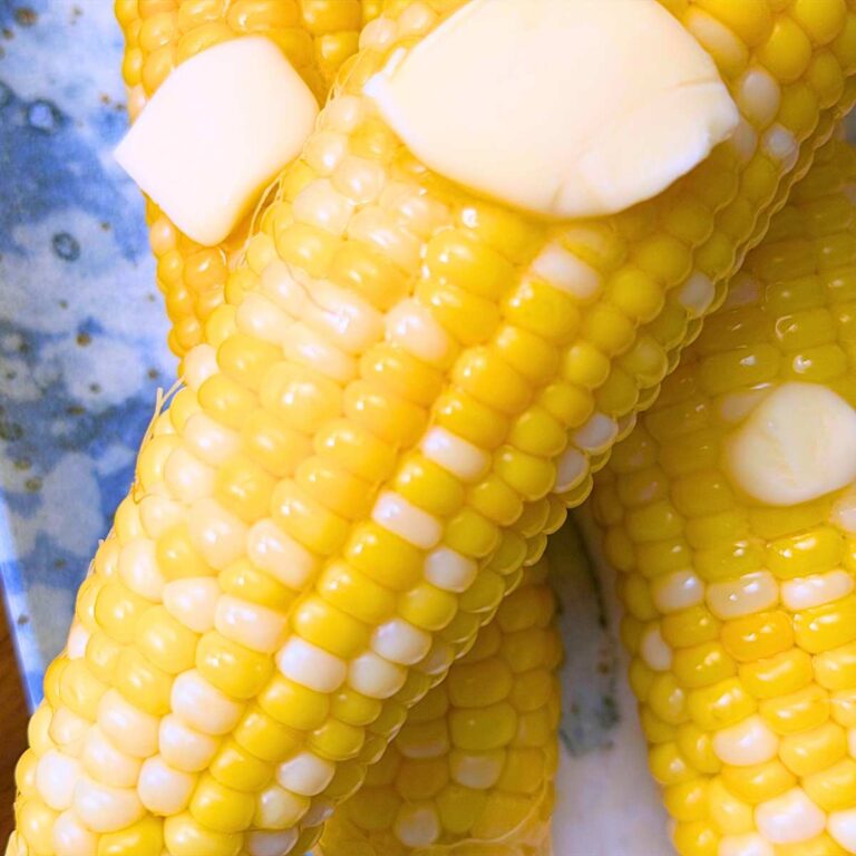 An overhead view of cooked corn on the cob with pats of butter on top.
