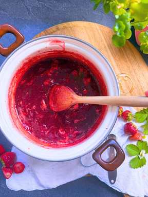 A white sauce pot filled with cooked strawberry jam.