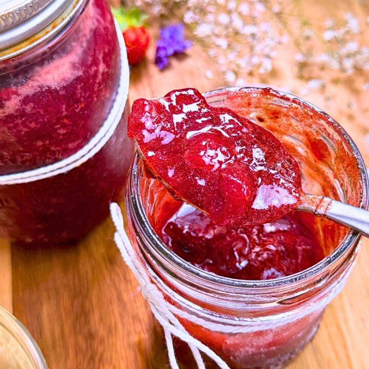 Two jars of strawberry jam. One is opened with a spoonful resting on top.