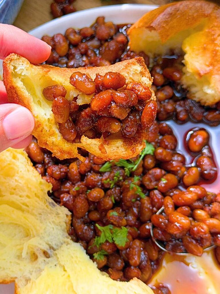 A woman is holding up a popover with some baked beans.
