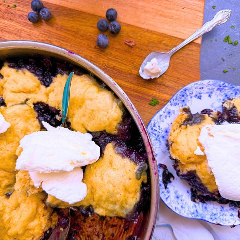 A metal pan with blueberry grunt inside. There is a serving off to the side with vanilla ice cream on top.