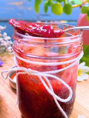 An opened jar of strawberry jam with a spoonful resting on top.
