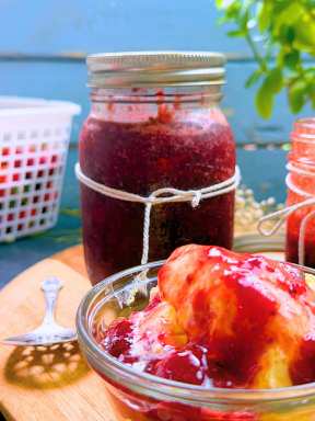Two jars of strawberry jam and a wooden bowl of vanilla ice cream with strawberry sauce on top.