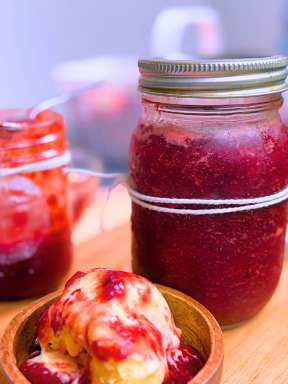 Two jars of strawberry jam and a wooden bowl of vanilla ice cream with strawberry sauce on top.