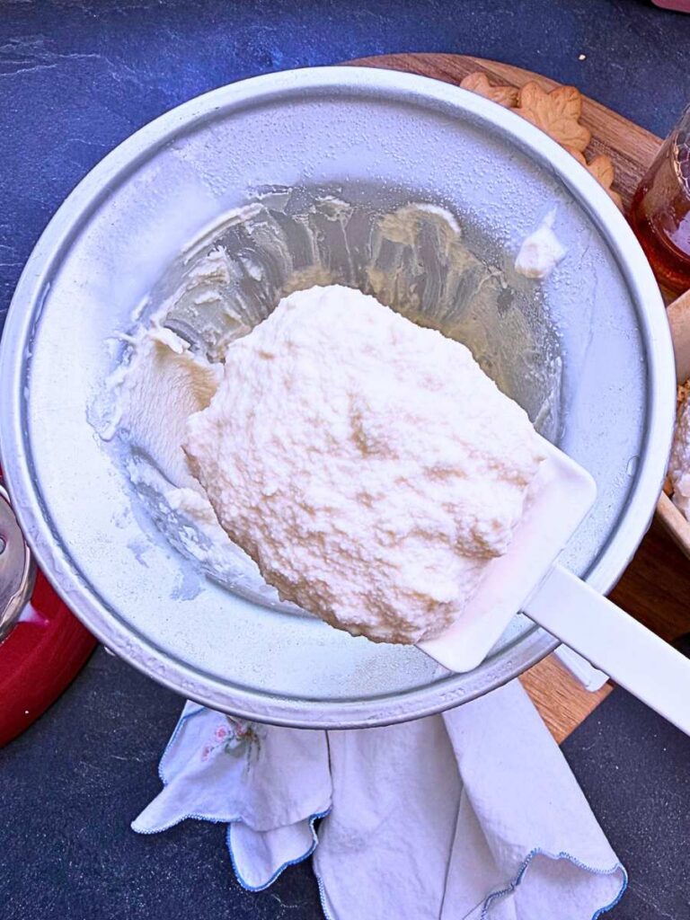 A woman holding up a scoop of churned maple ice cream.