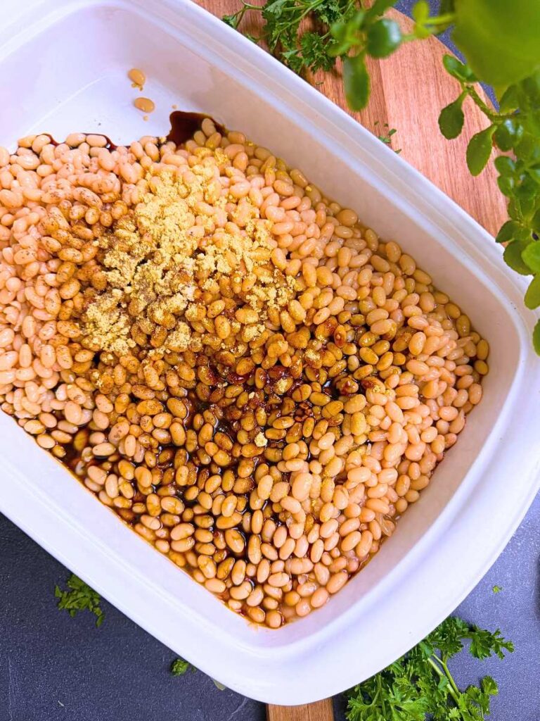 White navy beans in a white casserole dish. There is molasses and mustard powder on top.