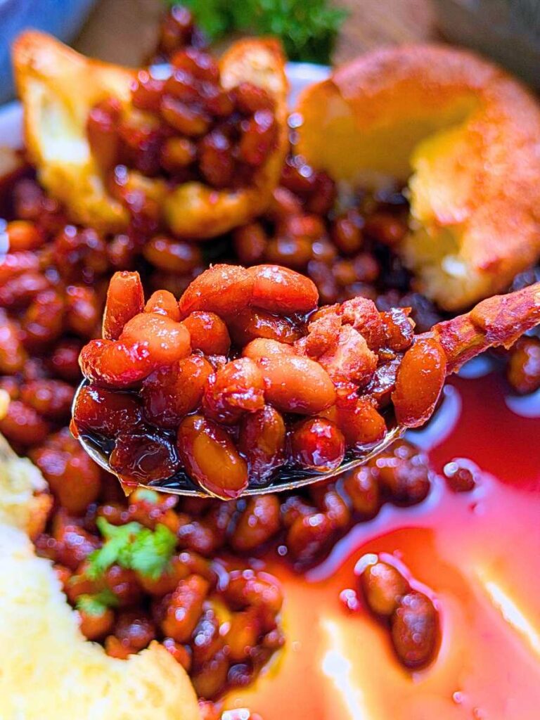 A woman is holding up a spoonful of baked beans.