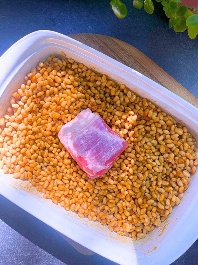 A white casserole dish filled with white navy beans and a salt pork in the centre.