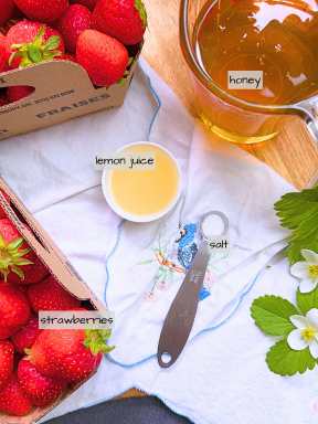 Fresh strawberries in cardboard boxes. There is a small cup of lemon juice, a spoon of salt, and a glass measuring cup of honey.