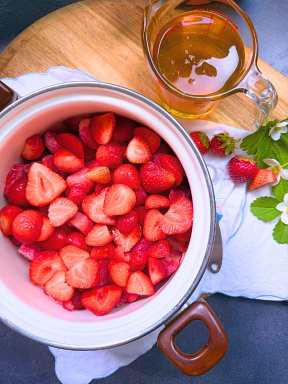 A white sauce pot filled with fresh strawberries cut in half.