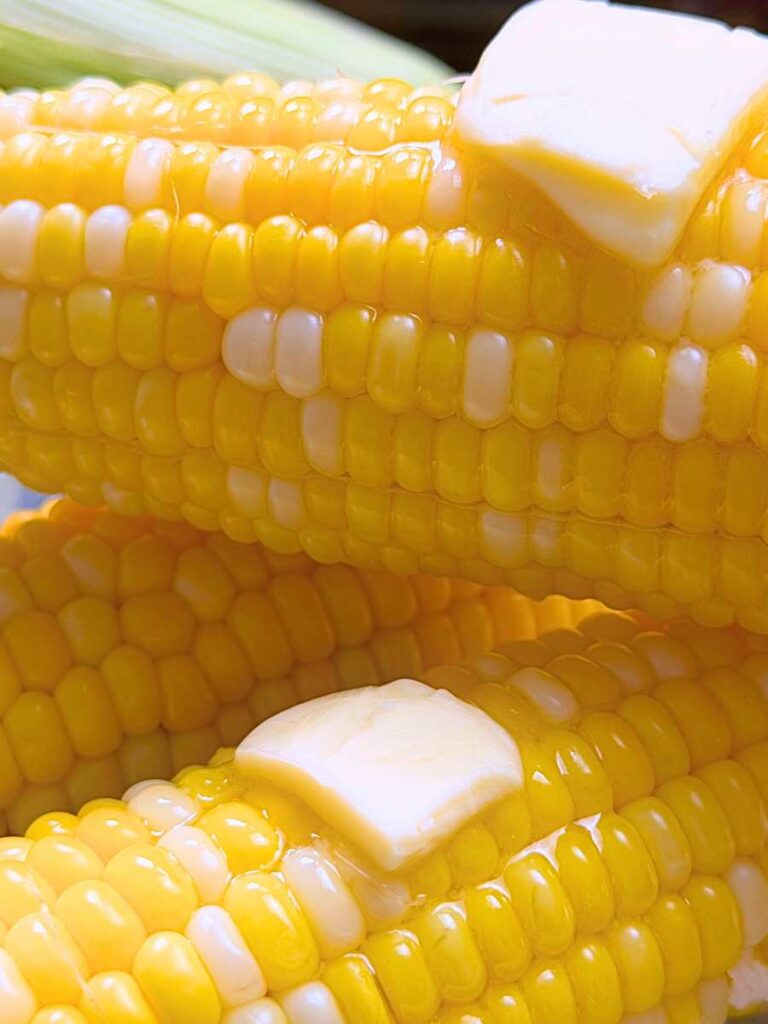 A side view of cooked corn on the cob with pats of butter on top.