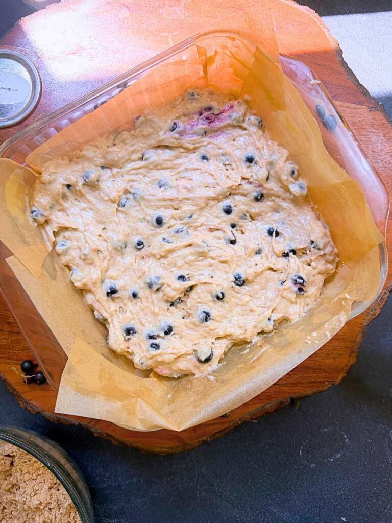 black current coffee cake batter in a lined square glass baking dish.