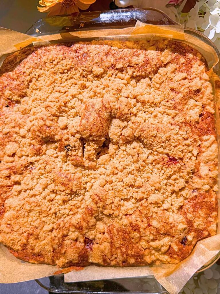 A baked black current coffee cake with a streusel topping in a glass square baking dish.