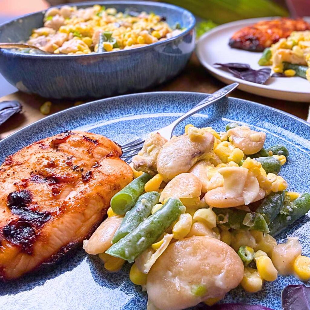 A blue plate with bean and corn succotash and barbecue chicken. There is more succotash in the background.