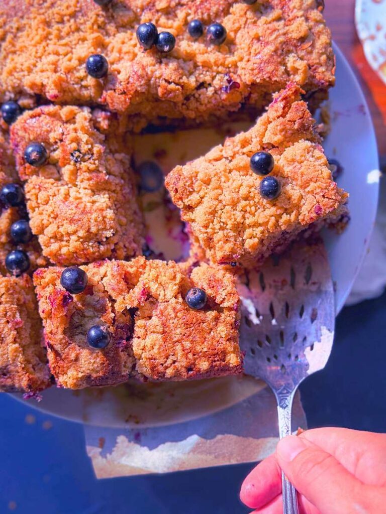 A woman is taking a slice of black current coffee cake with a metal spatula.