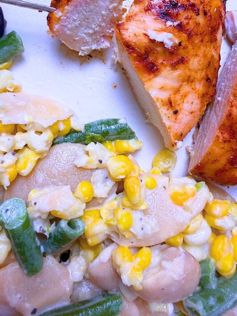 A white plate with corn and bean succotash and barbecue chicken.