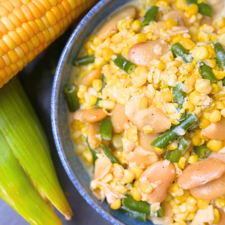 A blue bowl filled with corn and bean succotash. There is two ears of corn off to the side.