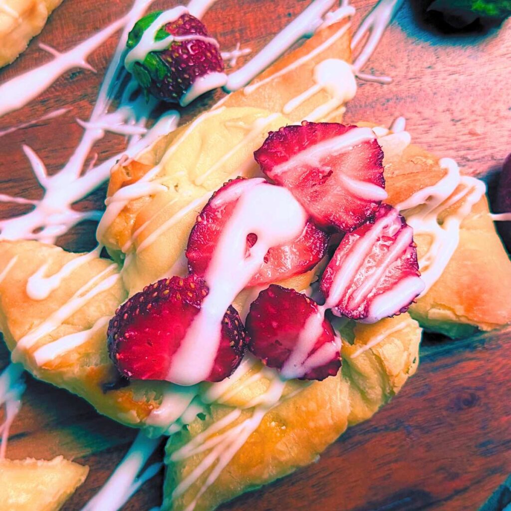 A sourdough cheese danish with sliced strawberries on top and a vanilla icing drizzle.