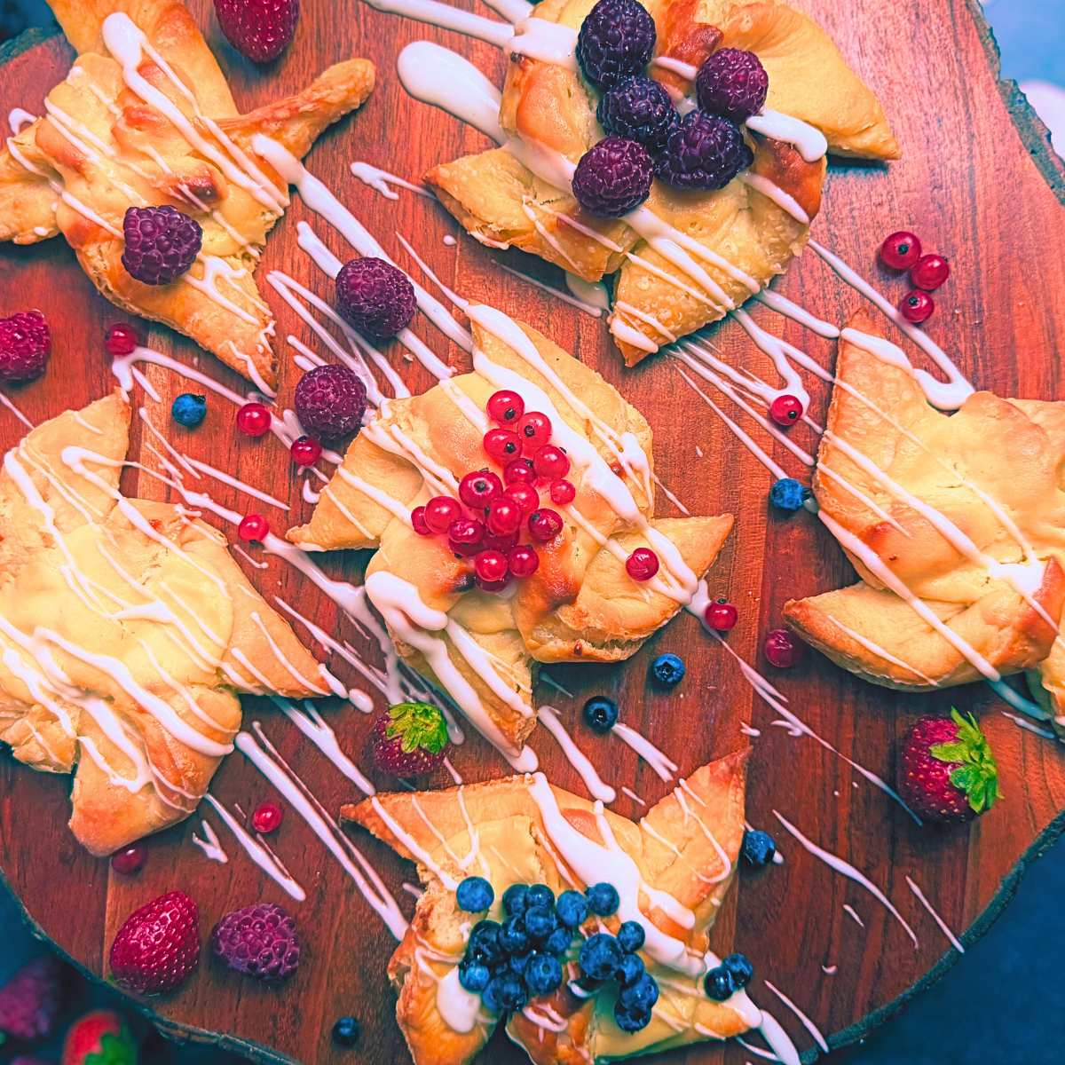 Sourdough cheese danishes on a wooden board. They are topped with assorted fresh fruit and a vanilla icing drizzle.