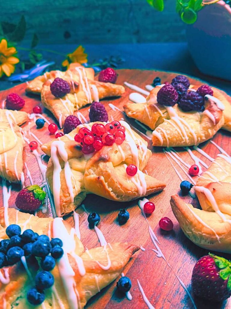 A collection of sourdough cheese danishes on a wooden board. They are topped with assorted berries.