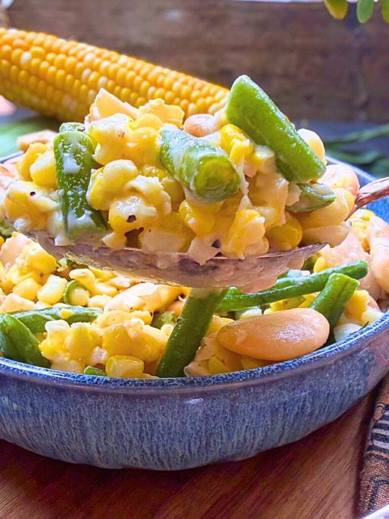 A blue bowl of creamy bean and corn succotash. A woman is holding up a large spoonful in front.
