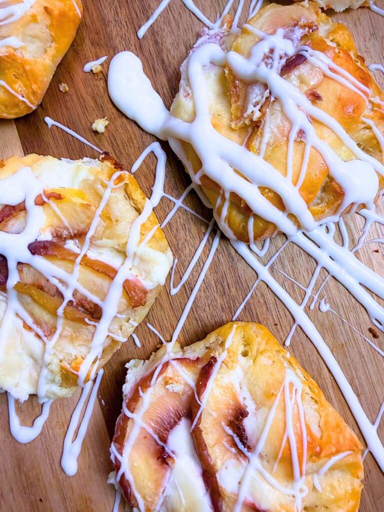 A collection of peach Danishes on a wooden board with a vanilla drizzle on top.