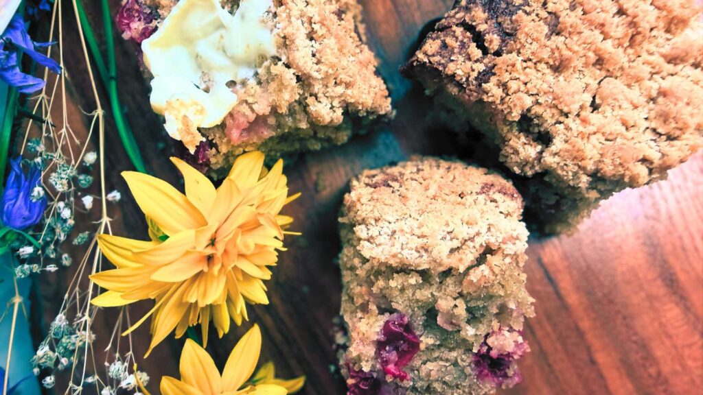 Three slices of gooseberry coffee cake. one is spread with butter. There are yellow flowers.