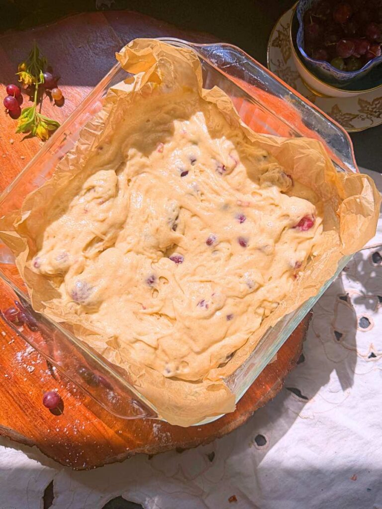 A glass baking dish lined with parchment paper with gooseberry coffee cake batter inside.