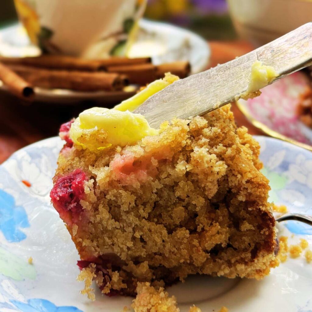 A woman is buttering a slice of gooseberry coffee cake.