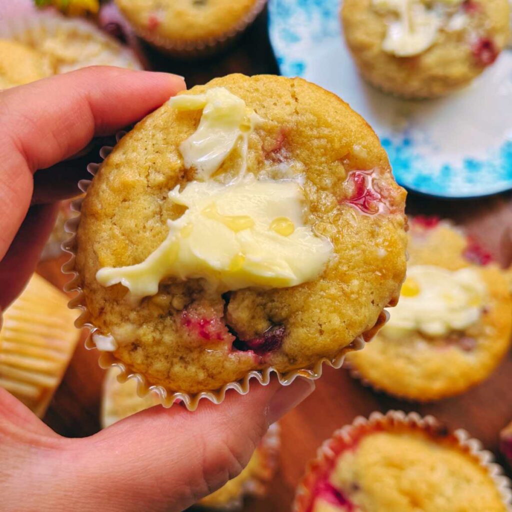 A woman is holding a gooseberry muffin with butter spread on top.