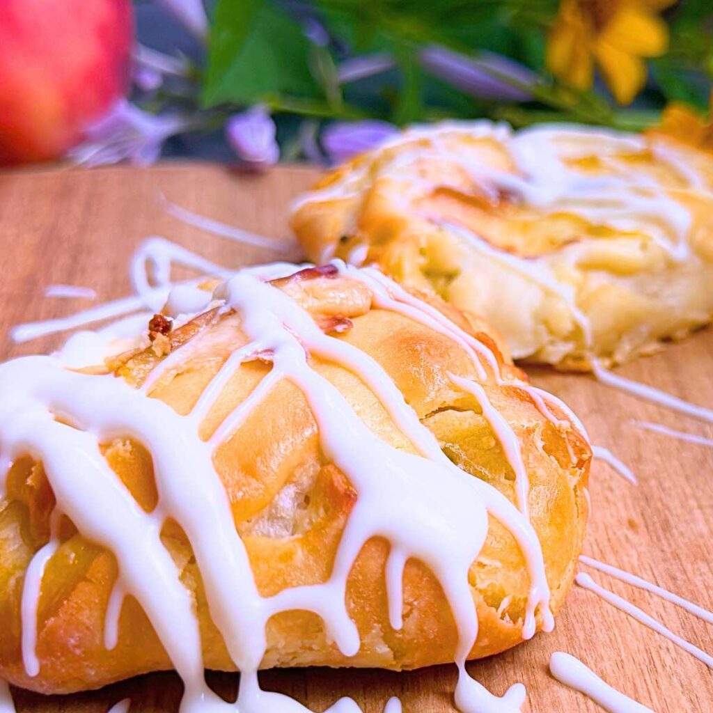 A side view of a peach Danish with a white drizzle on top. There are more in the background.