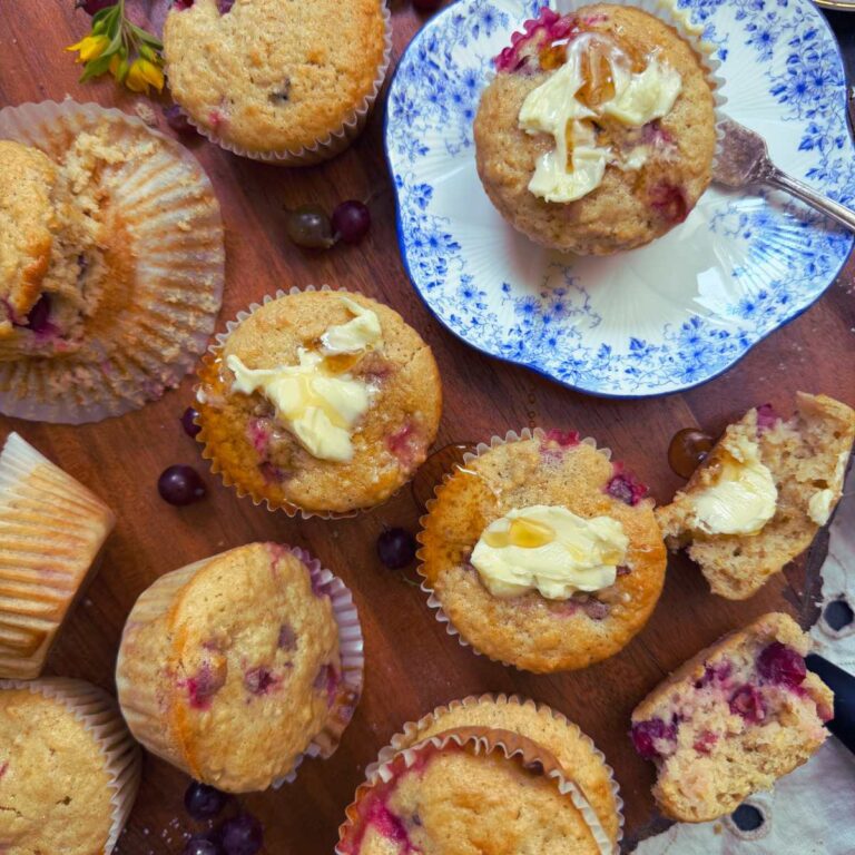 A collection of gooseberry muffins on a wooden board. Some are spread with butter. One is on a blue plate.
