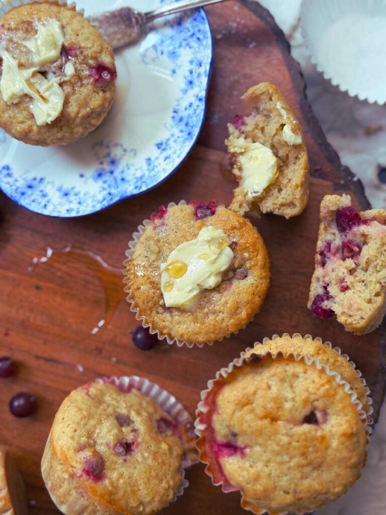 Gooseberry muffins on a wooden board. There is one on a blue plate behind. Some are spread with butter.