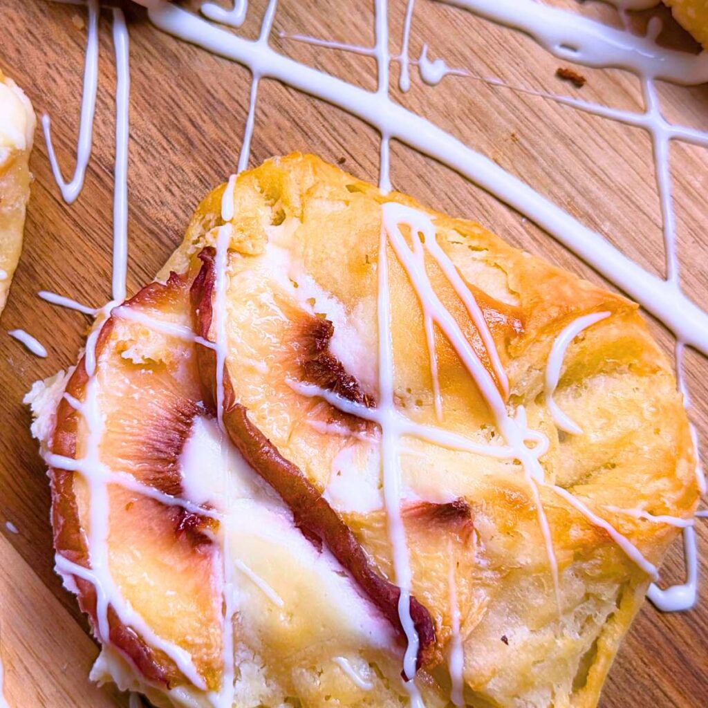 A Danish with sliced peaches on top. There is a vanilla drizzle on the Danish.