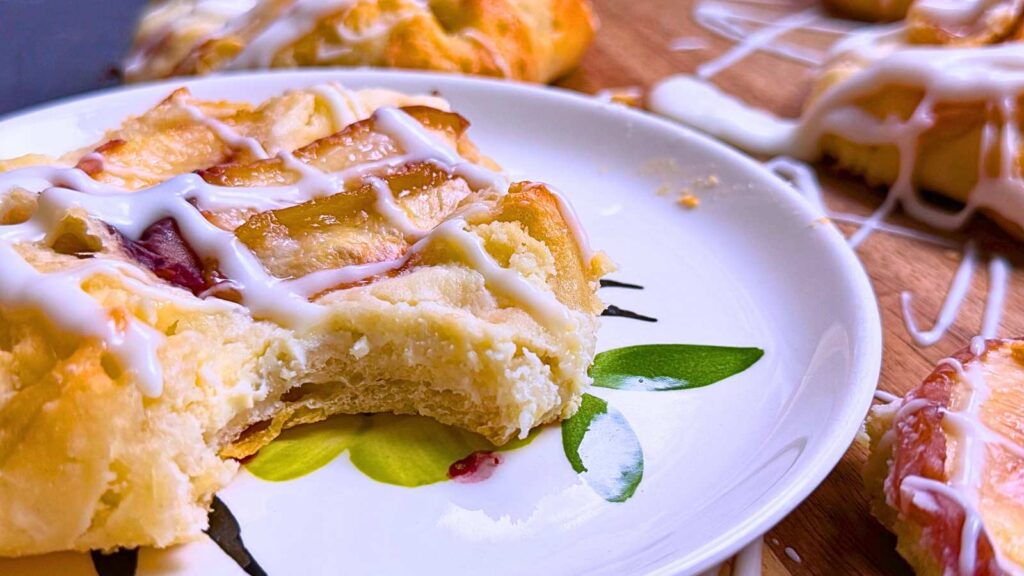 A white plate with a cheese and peach Danish. There is a bite out of it.