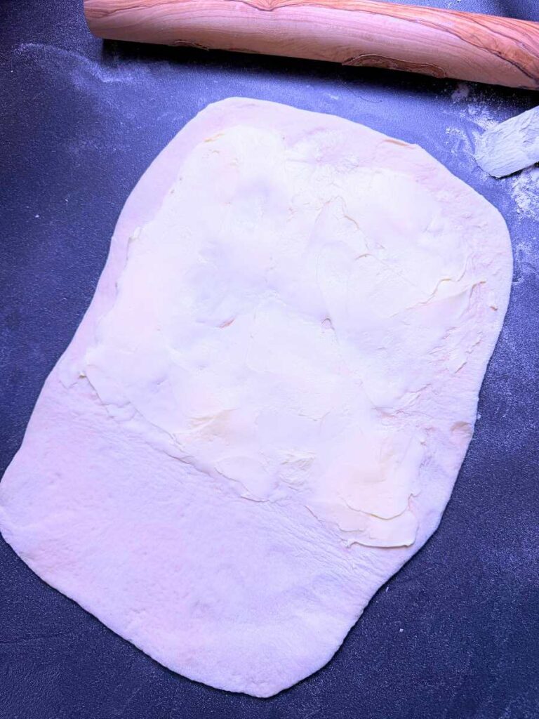 A rectangle of dough with butter spread out on 2/3 of it.