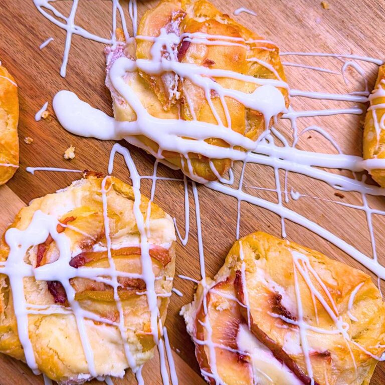 Peach Danishes with a vanilla drizzle on a wooden board.