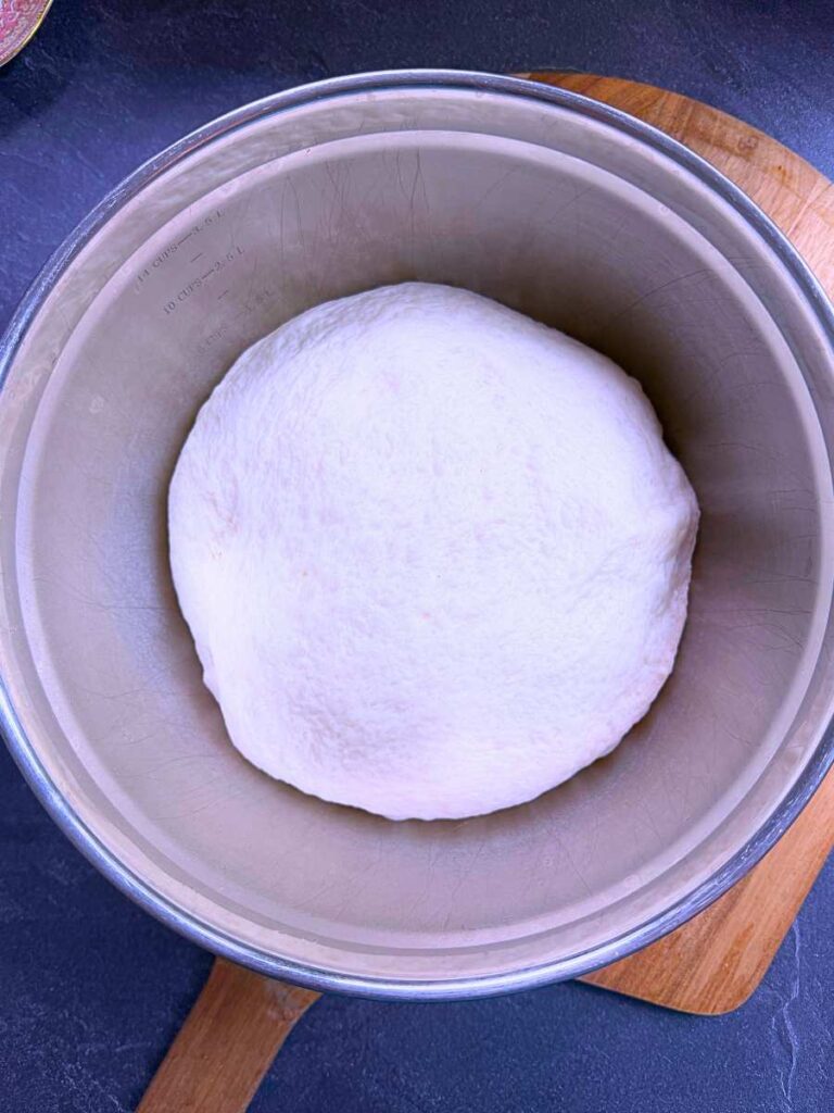 A metal bowl with risen dough inside.