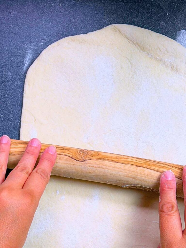 A woman is rolling out dough with a wooden rolling pin.