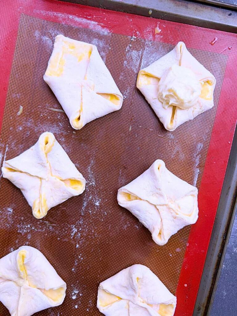 Danish dough shaped into folded squares. One has cream cheese filling on top.