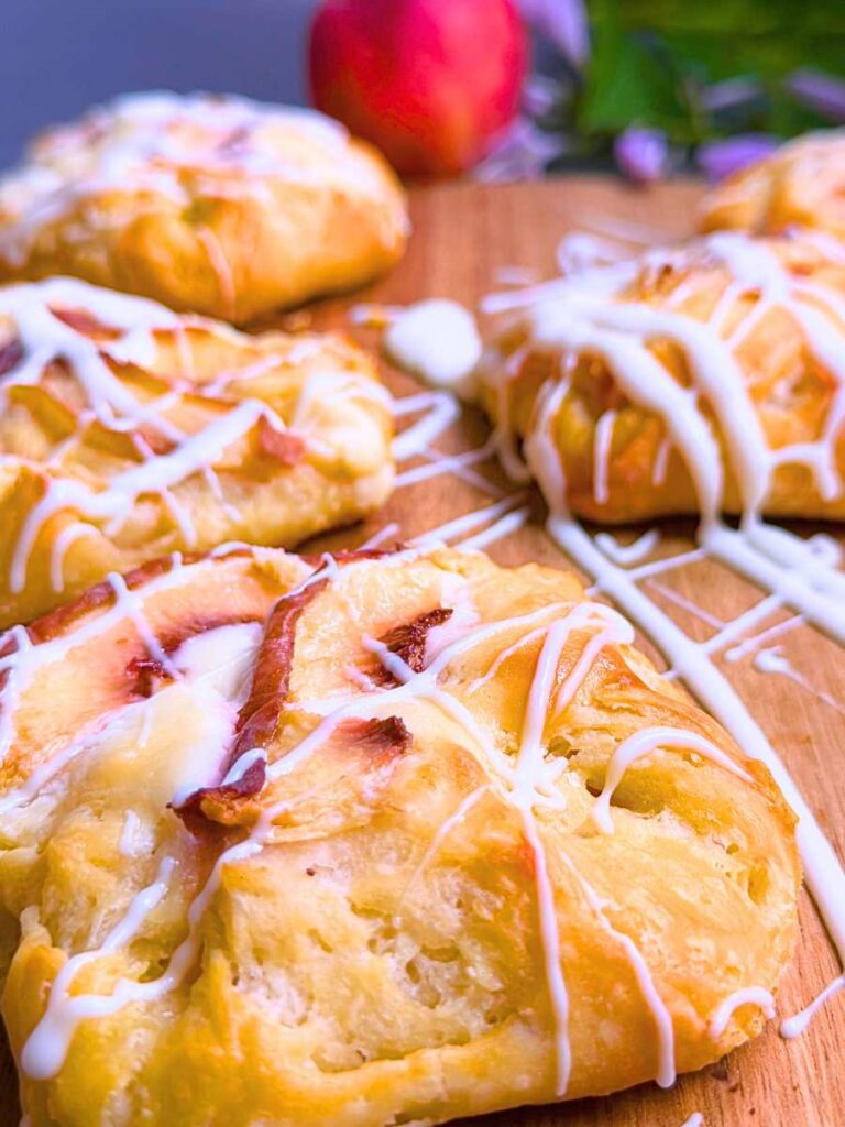 A side view of a Danish with sliced peaches on top. There are more pastries in the background.